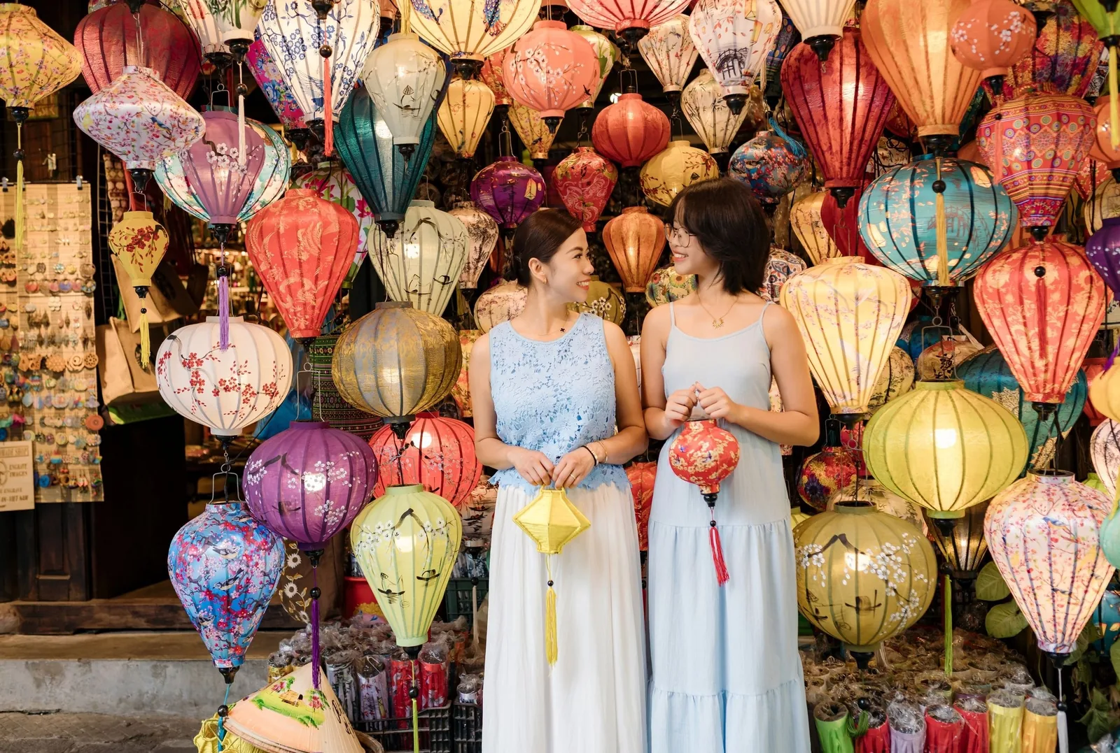 Two women in blue dresses browse colorful silk lanterns at a shop in Hoi An.